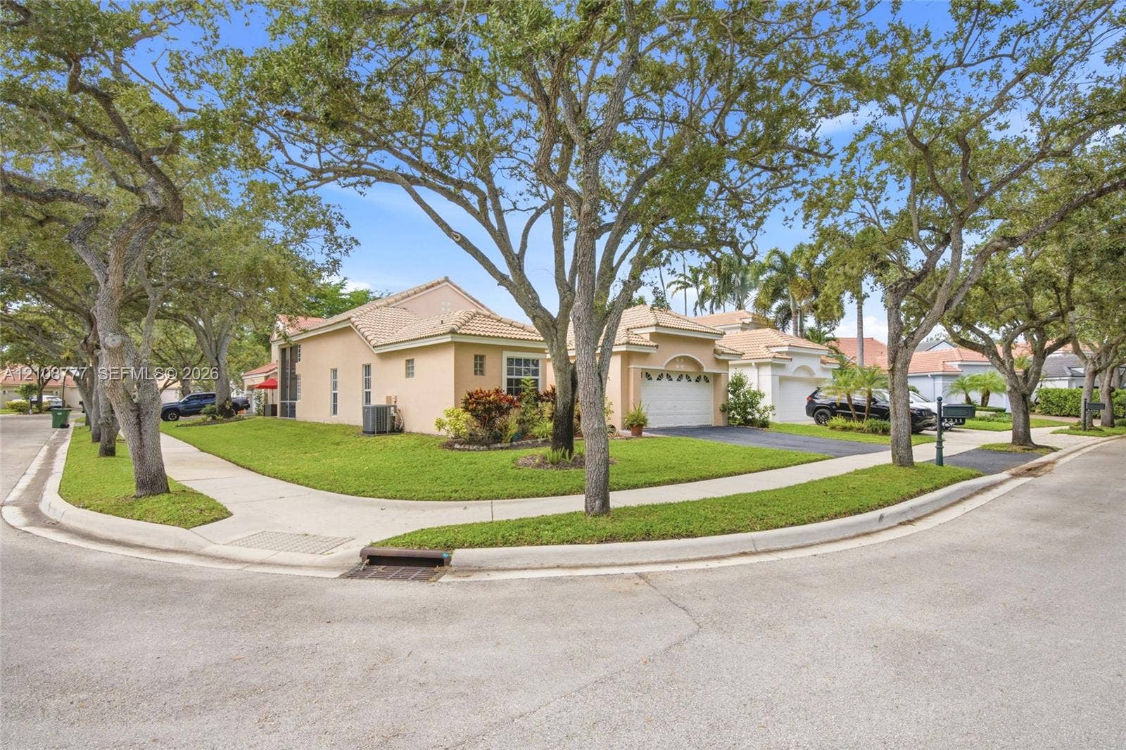 Exterior facade featuring a stucco finish, multi-gable tile roof, attached garage, and mature shade trees on a corner lot