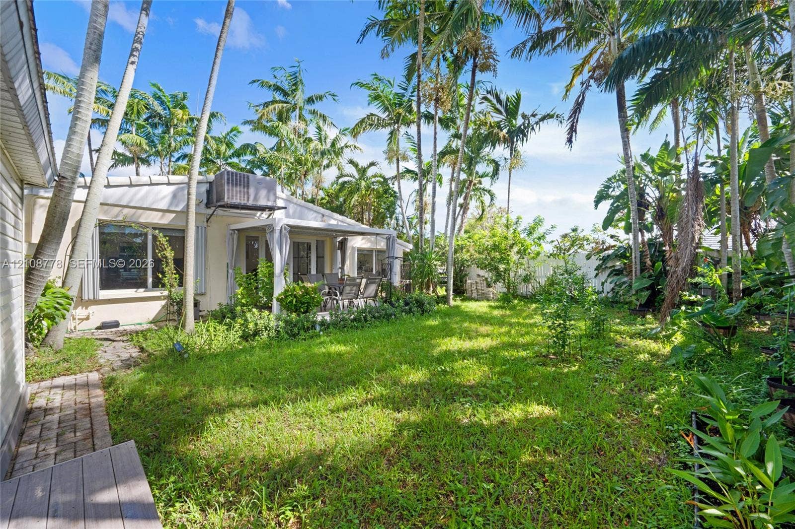 3116 Hayes Street, Hollywood, FL 33021 Expansive backyard featuring a lush lawn, mature palm trees, a covered patio, and brick paver pathways