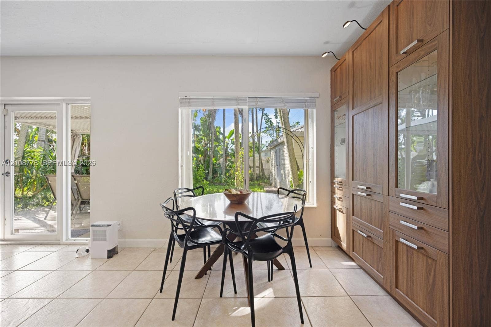 3116 Hayes Street, Hollywood, FL 33021 Full-wall wood cabinetry featuring integrated storage, glass-front display sections, and overhead directional lighting, complemented by tile flooring, a large picture window, and a glass-panel exterior door
