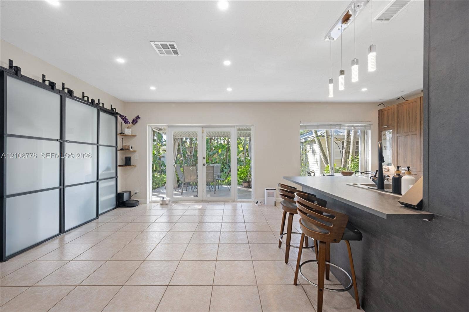 3116 Hayes Street, Hollywood, FL 33021 Large-format tile flooring, oversized matte black sliding partition with frosted glass panels, kitchen island with breakfast bar seating, and linear pendant lighting