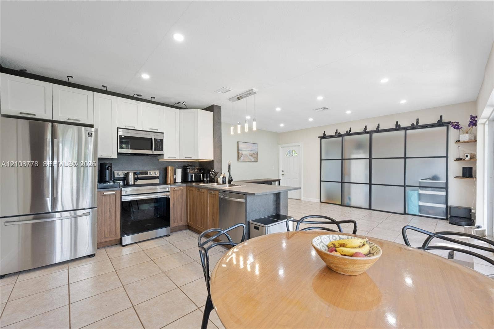 3116 Hayes Street, Hollywood, FL 33021 Kitchen featuring dual-tone cabinetry, stainless steel appliances, a peninsula with stone-surface countertop, recessed lighting, and large frosted-glass sliding doors with metal framing
