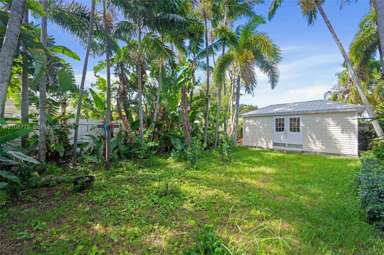 3116 Hayes Street, Hollywood, FL 33021 Backyard featuring mature palm trees, a detached structure with a metal roof, and white vinyl perimeter fencing