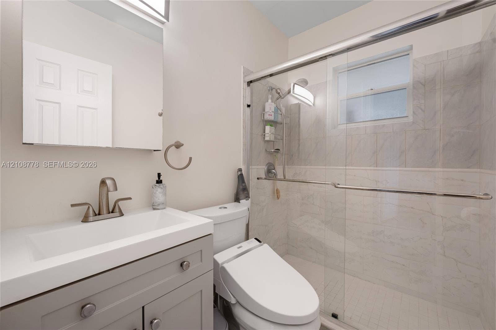 3116 Hayes Street, Hollywood, FL 33021 Bathroom featuring a gray vanity with a white rectangular sink, a glass-enclosed shower with tiled surround, and a wall-mounted medicine cabinet