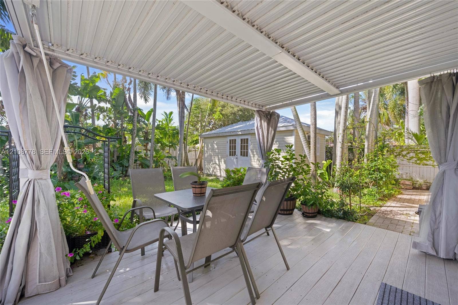 3116 Hayes Street, Hollywood, FL 33021 Covered deck with light-toned wood-finish flooring, metal pergola structure, and detached exterior storage building set within a mature landscape