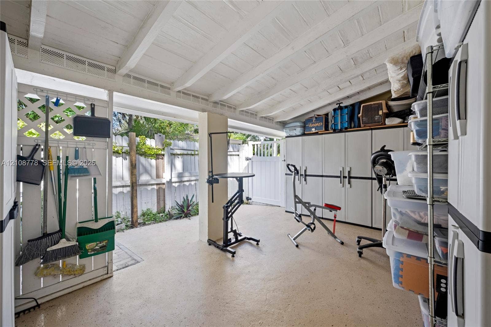 3116 Hayes Street, Hollywood, FL 33021 Covered patio area featuring a white-painted exposed beam ceiling, concrete flooring, lattice wall paneling, and a secured gate