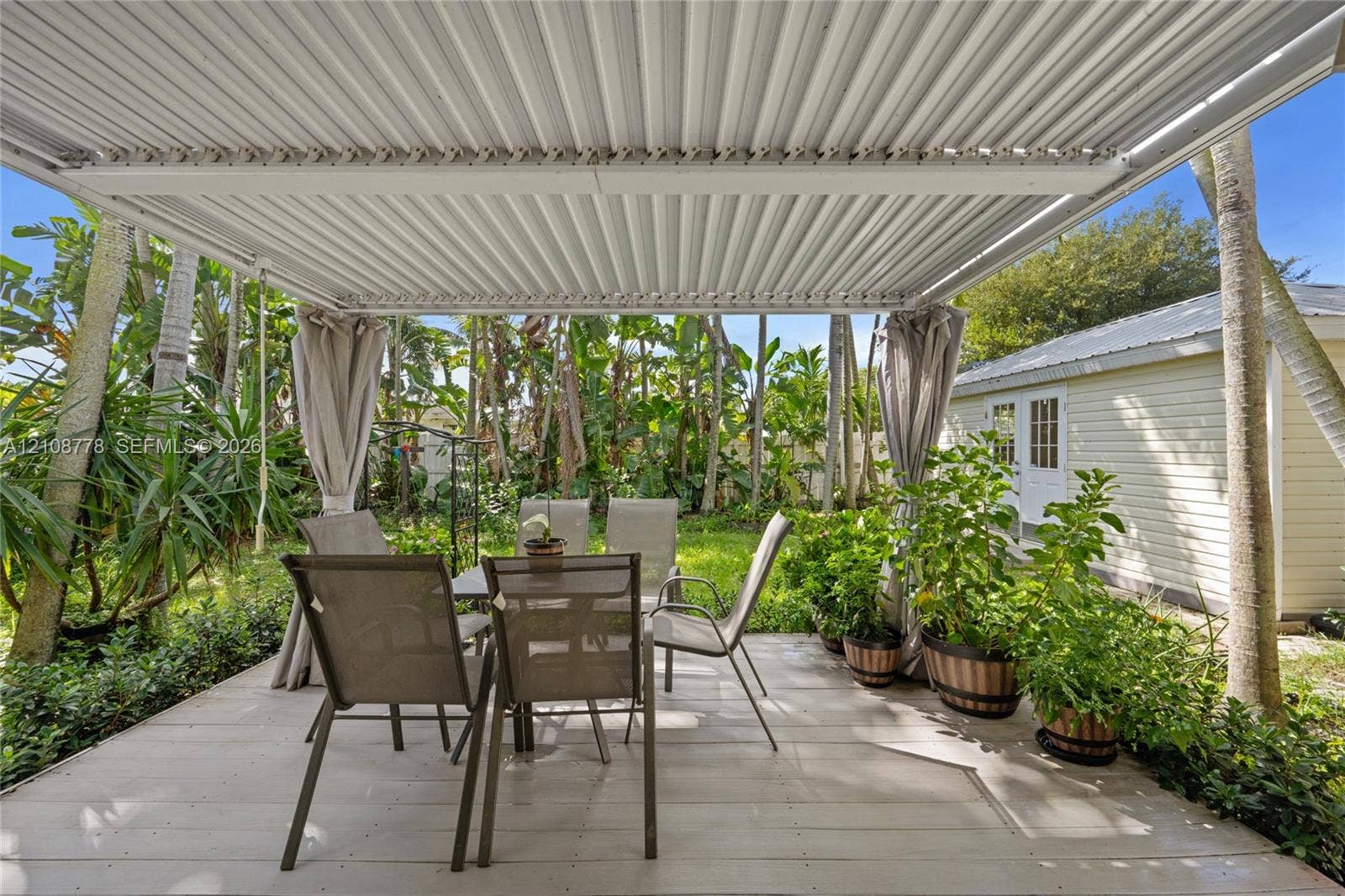 3116 Hayes Street, Hollywood, FL 33021 Covered patio with a corrugated metal roof structure, wood-plank style decking, and mature tropical landscaping