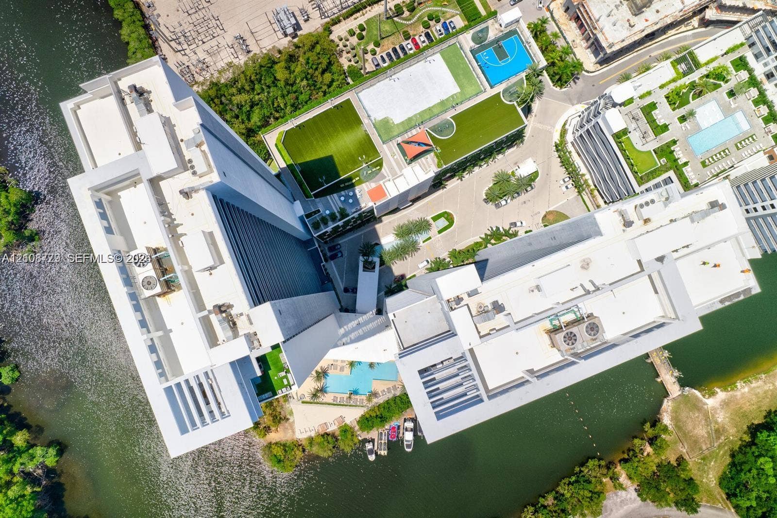 Aerial perspective of high-rise structure featuring waterfront access, outdoor swimming pool, basketball court, soccer field, and landscaped grounds