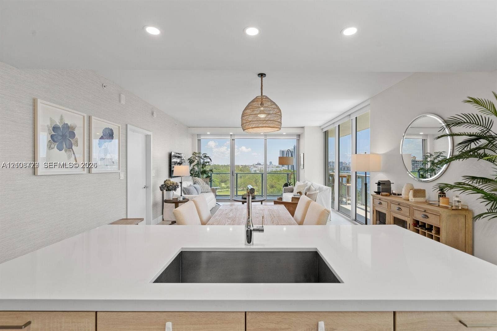 Kitchen island featuring a solid-surface countertop, under-mount stainless steel sink, and light wood-finish cabinetry, complemented by recessed ceiling lighting and floor-to-ceiling glass sliding doors