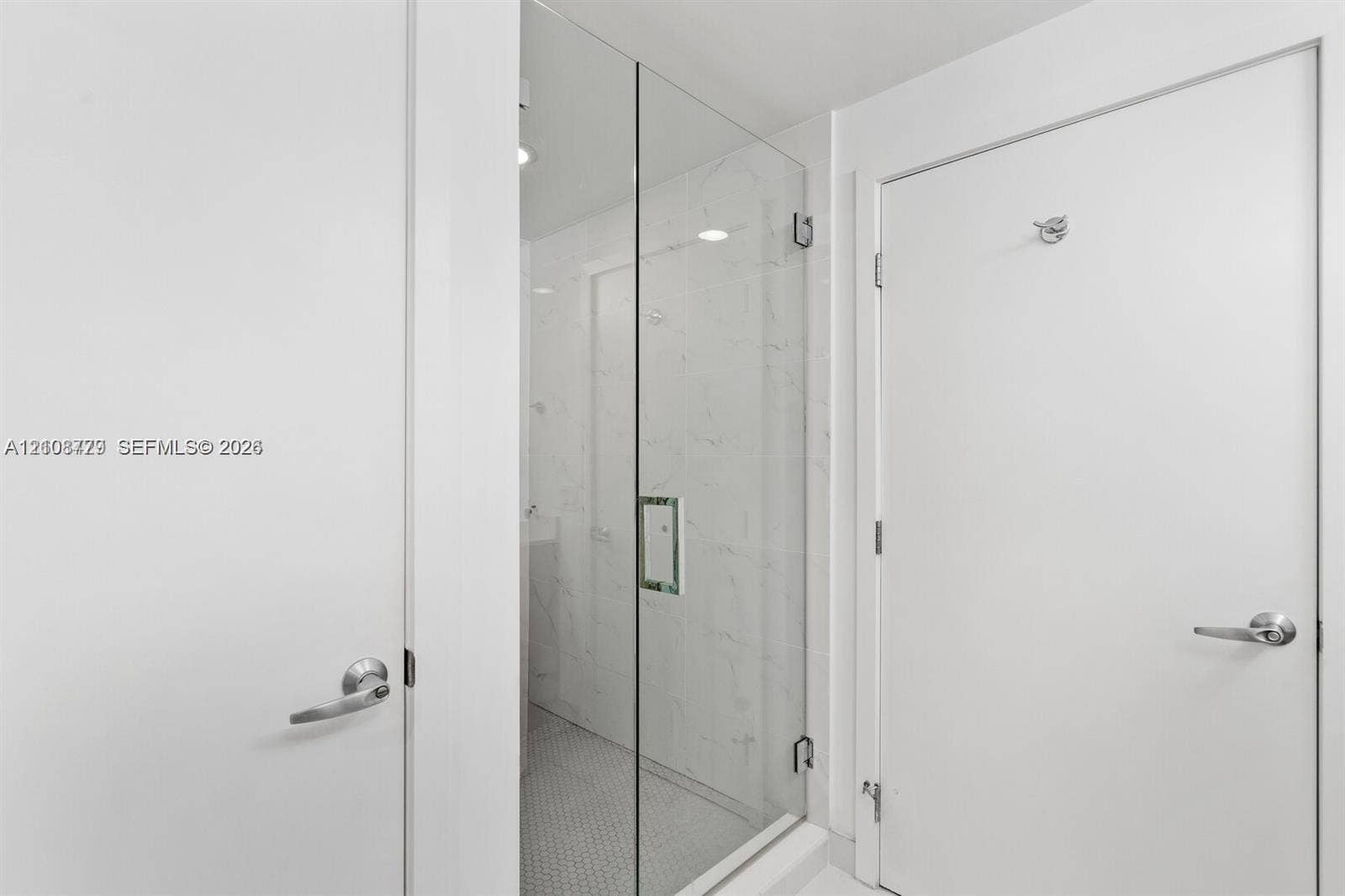 Walk-in shower featuring a frameless glass door, light-toned stone-finish tile surround, and mosaic floor tiling