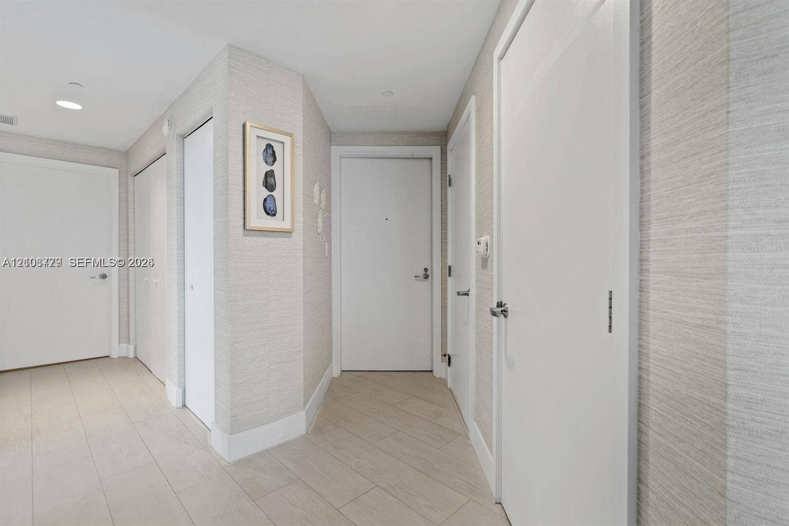 Entryway featuring neutral-toned textured wall covering, large-format tile flooring, multiple interior doors with brushed metal hardware, and recessed ceiling lighting