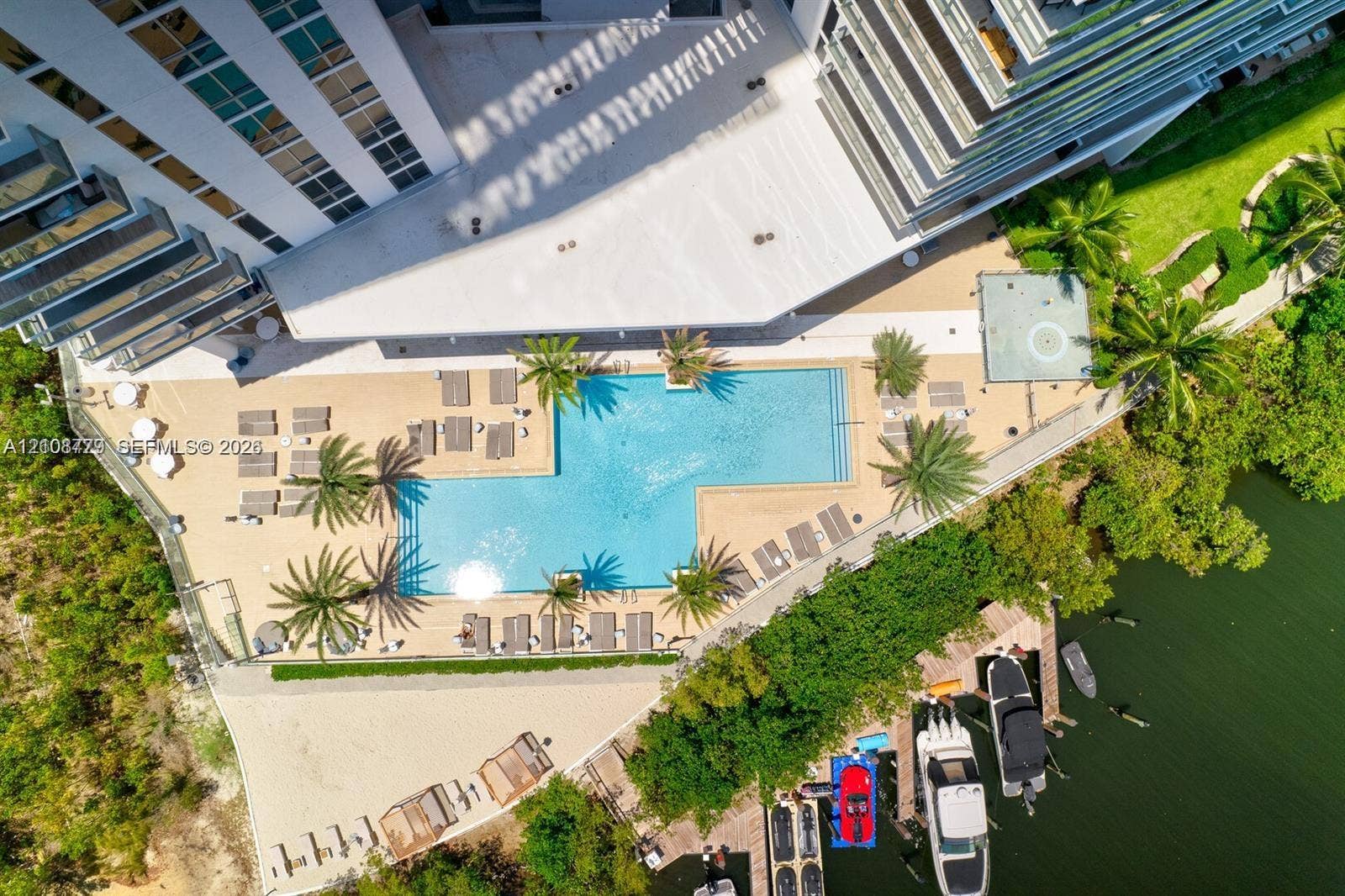 Aerial perspective featuring a swimming pool, paved sundeck, tropical landscaping, and private boat slips along the shoreline