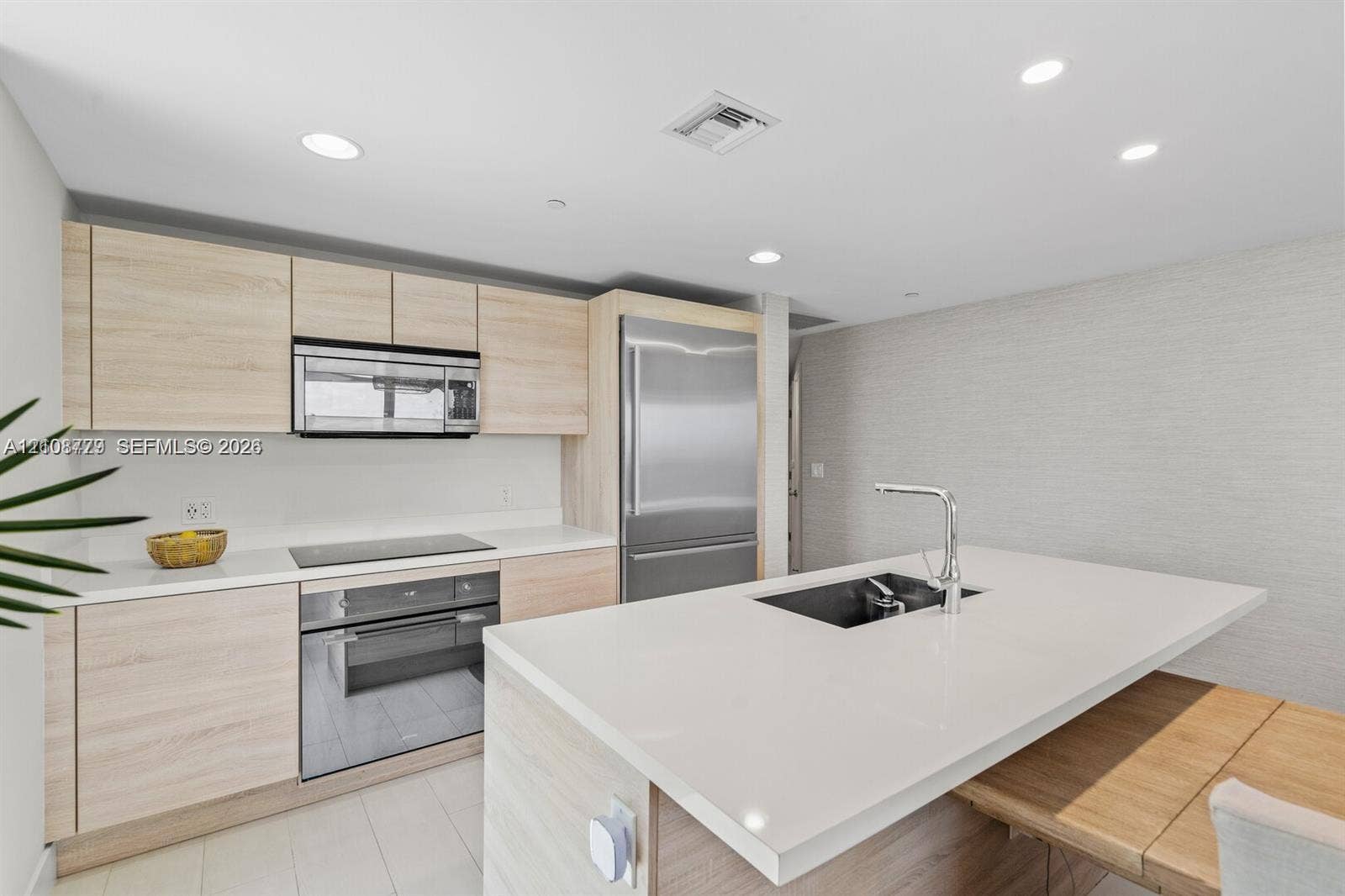 Kitchen featuring light wood-finish cabinetry, quartz countertops, a central island with an undermount sink and chrome faucet, recessed lighting, and stainless-steel appliances