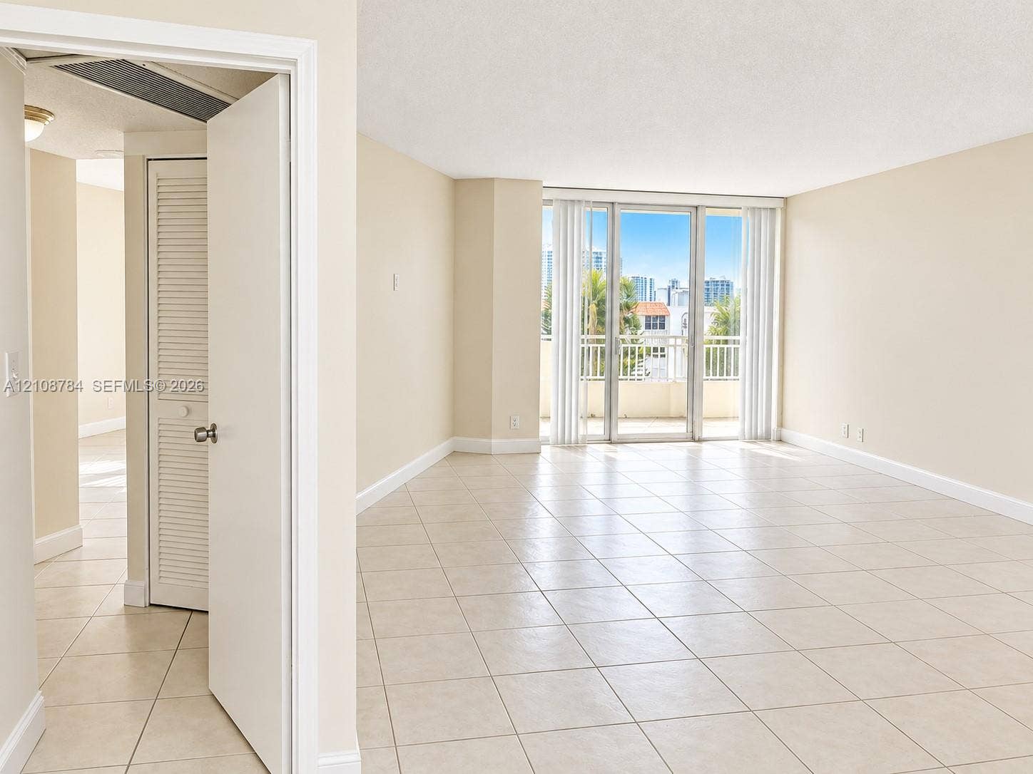 Open-concept room featuring light-colored ceramic tile flooring, floor-to-ceiling glass sliding doors, a metal-railed balcony, and louvered bifold closet doors