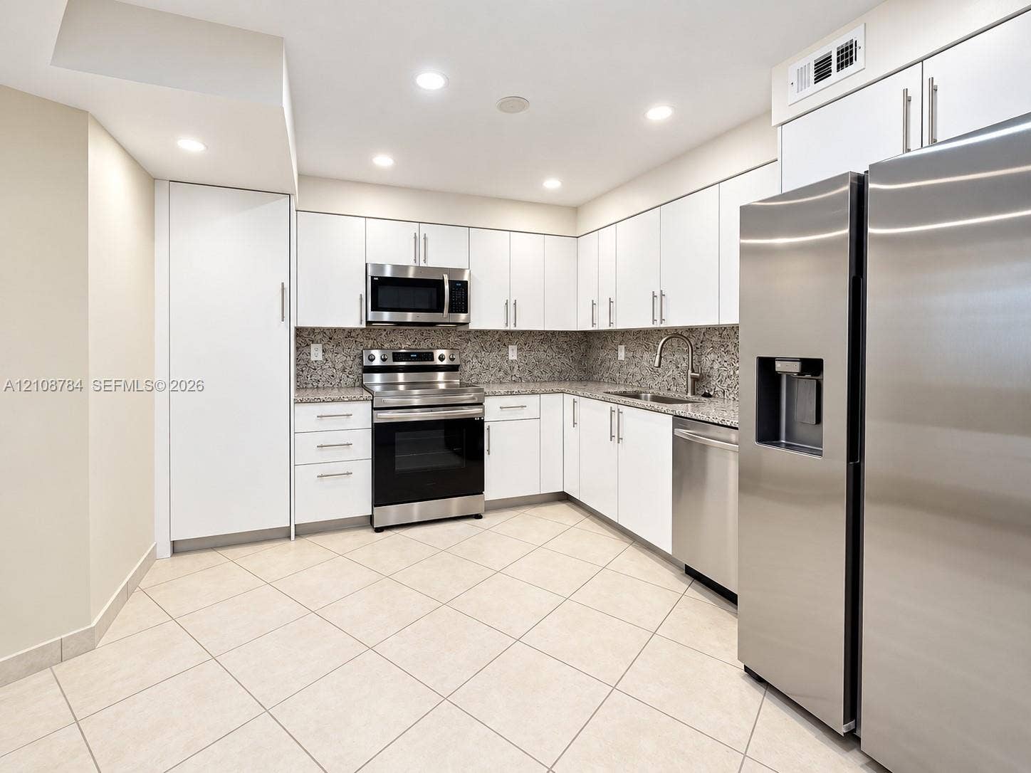 Kitchen featuring white cabinetry, stone-finish countertops, stainless steel appliances, a double-basin undermount sink, and tile flooring