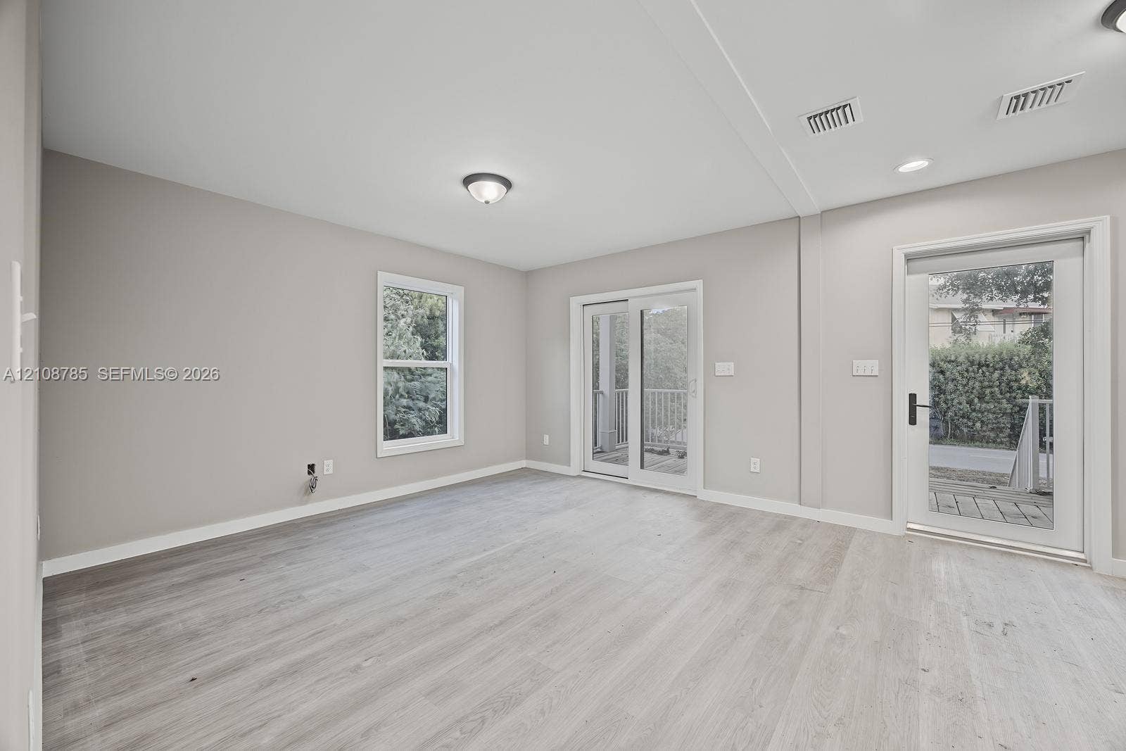 Neutral-toned interior space featuring wood-finish flooring, sliding glass patio doors, a separate exterior door with a glass pane, and recessed ceiling lighting