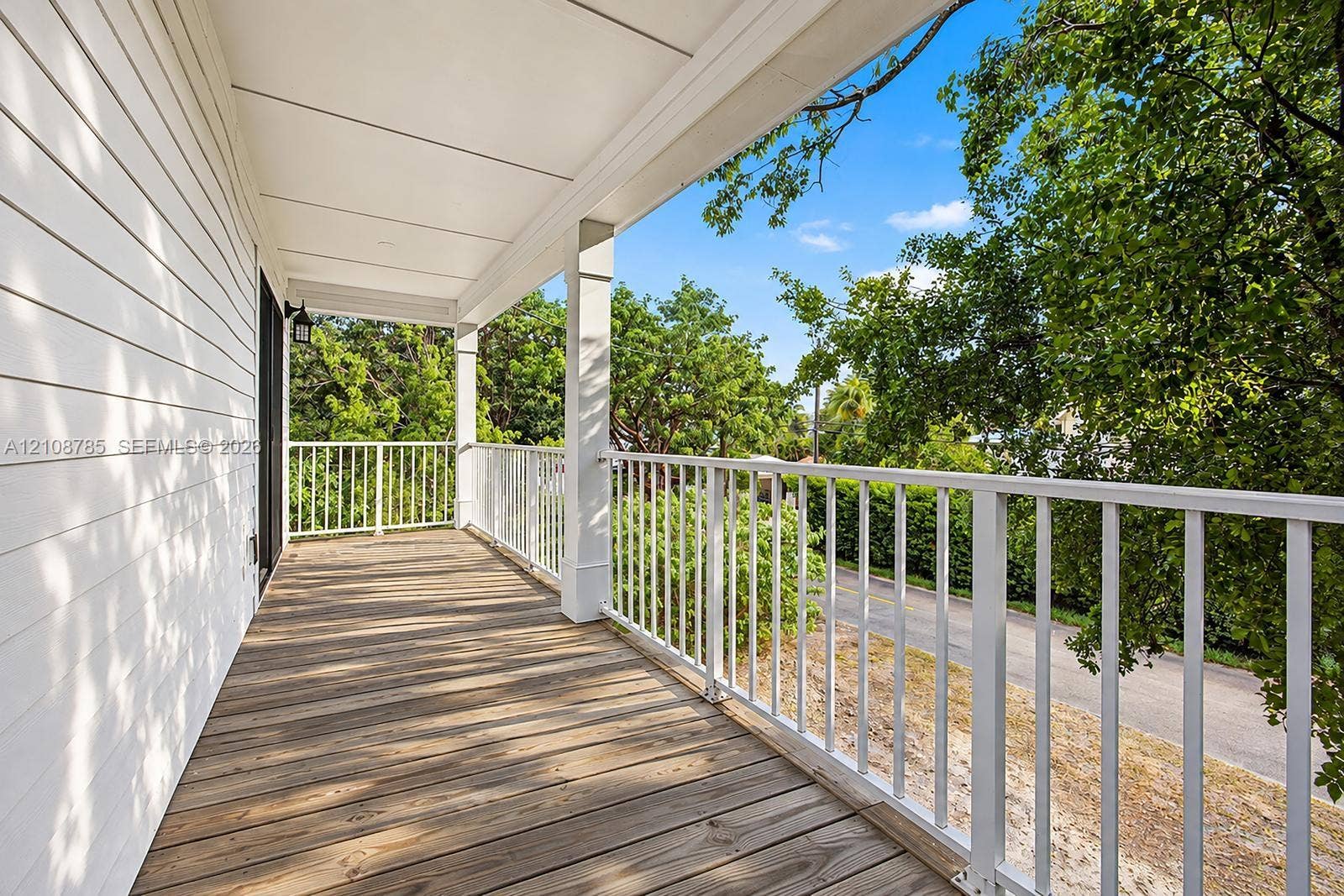 Covered deck featuring wood-finish decking, white metal railing, and white horizontal siding