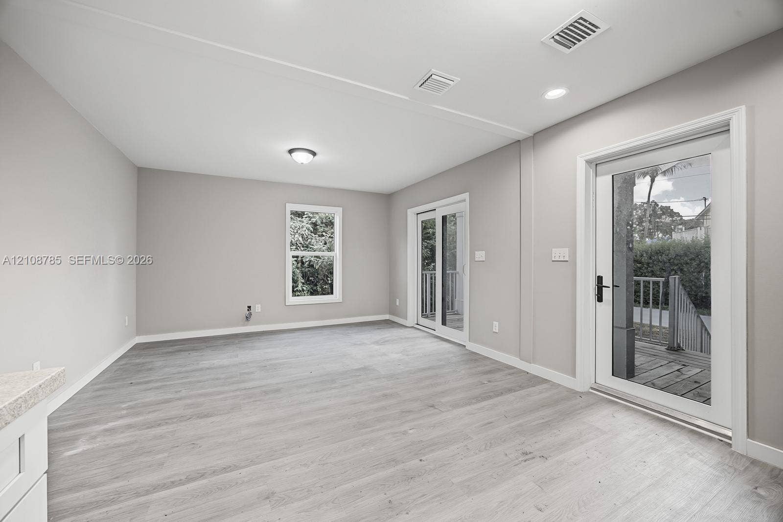 Neutral interior featuring wood-finish flooring, recessed lighting, double glass sliding doors, and a window with exterior greenery
