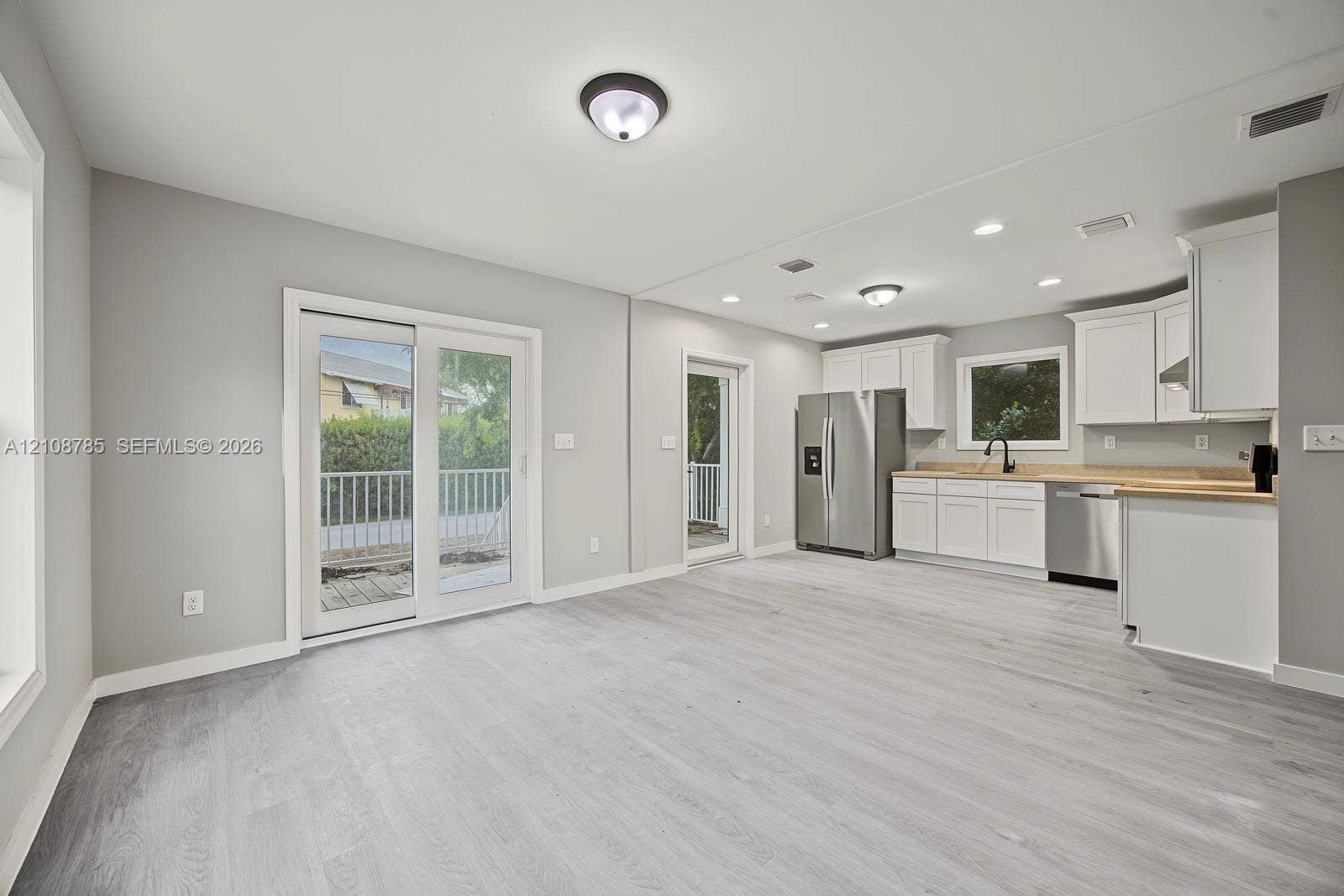 Open-concept space featuring wood-finish flooring, white shaker cabinetry, stainless steel appliances, neutral wall color, and glass sliding door access