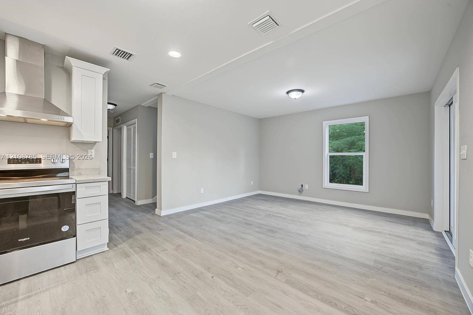 Kitchen featuring stainless steel range, professional-grade range hood, white cabinetry, and wood-finish flooring