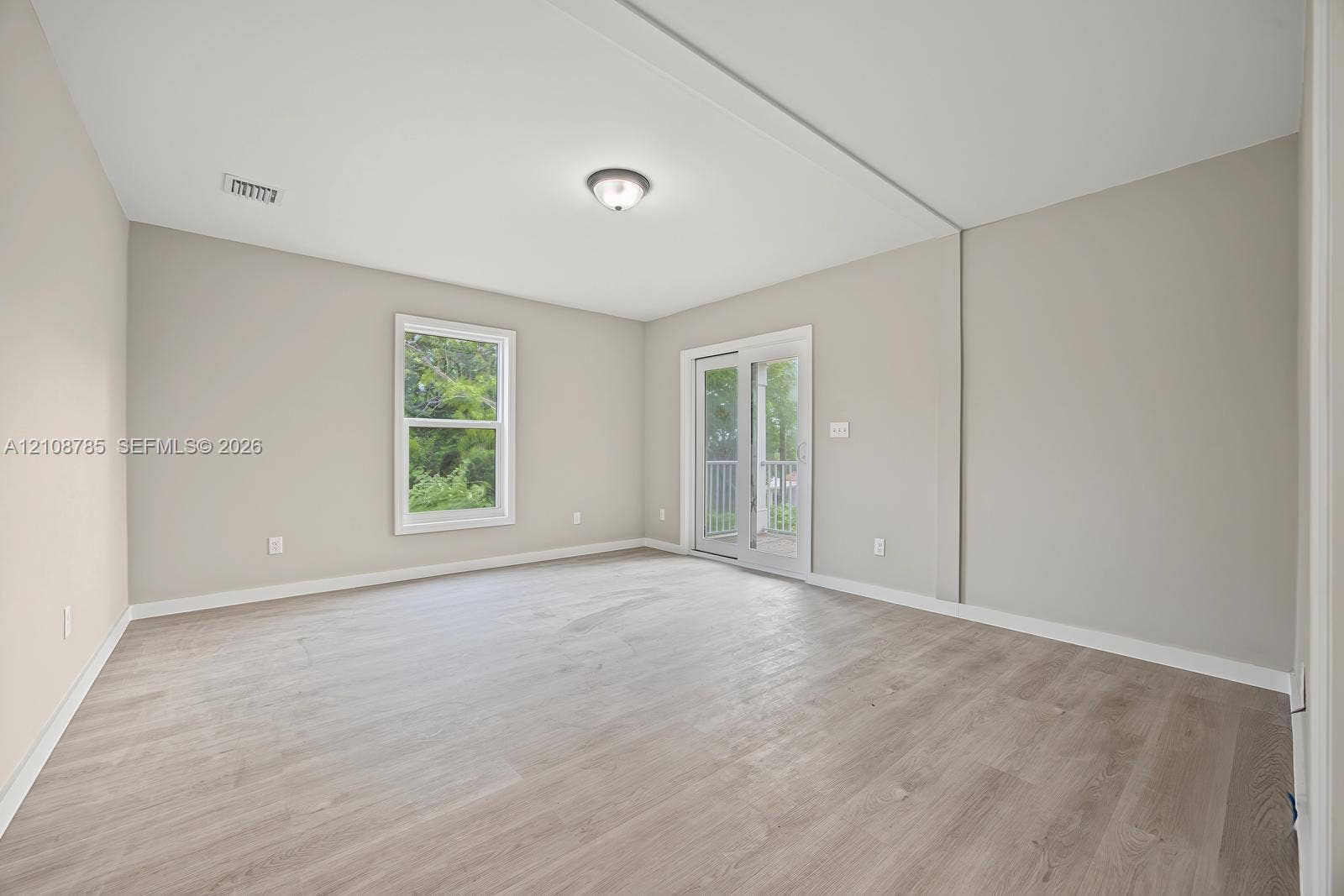 Neutral-toned interior featuring wood-finish flooring, a glass-pane sliding door with exterior access, a single window, and a flush-mount ceiling light fixture