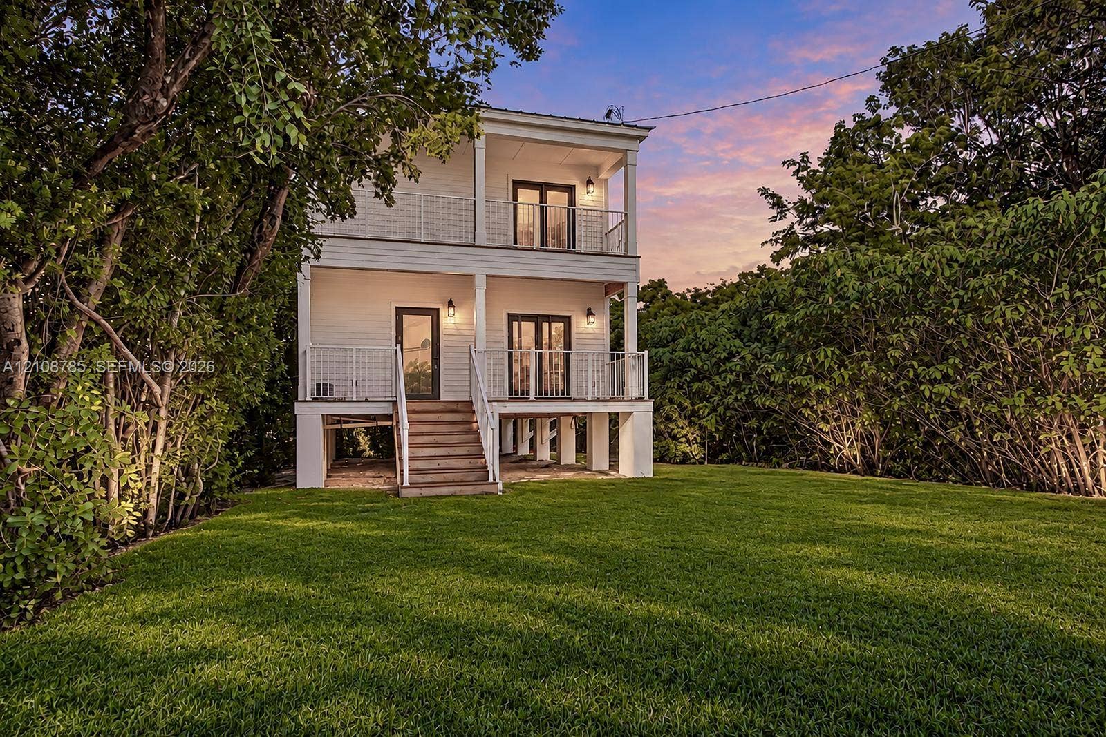 Two-story exterior featuring white horizontal siding, double-level covered porches with metal railings, a raised pier foundation, and glass-paneled exterior doors