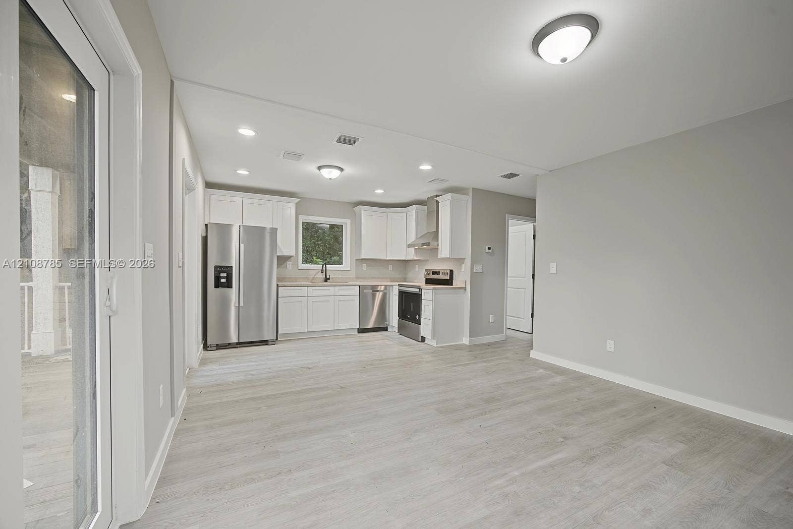 Kitchen featuring white cabinetry, stainless steel appliances, wood-finish flooring, recessed lighting, and a sliding glass door
