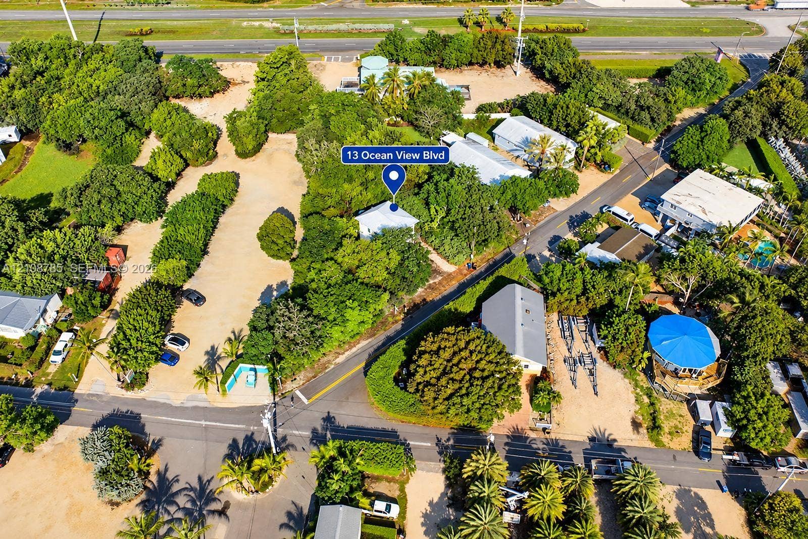 Expansive corner lot featuring mature trees, established landscaping, and a gravel parking area