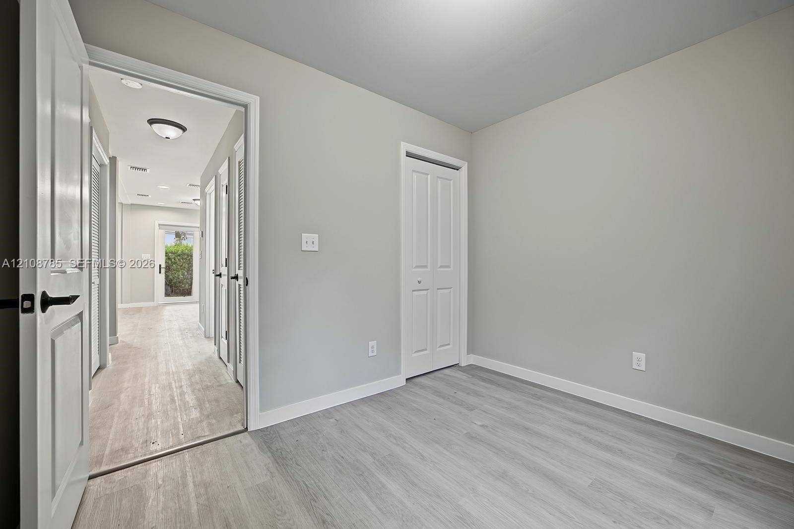 Interior space featuring neutral-toned walls, wood-finish flooring, and white paneled doors with matte black hardware