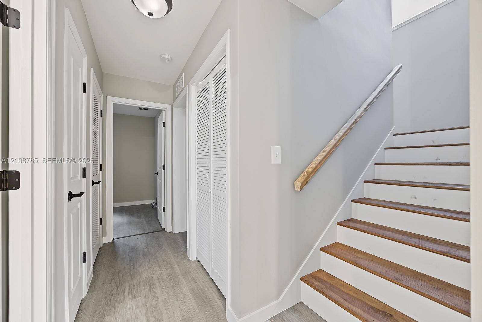 Staircase featuring wood-finish treads and a natural wood handrail, paired with interior doors showcasing matte black hardware and white louvered closet doors