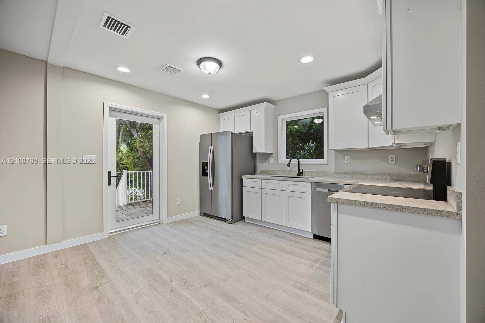Kitchen featuring white cabinetry, stone-finish countertops, stainless steel appliances, a deep-basin sink with a matte black faucet, and wood-finish flooring