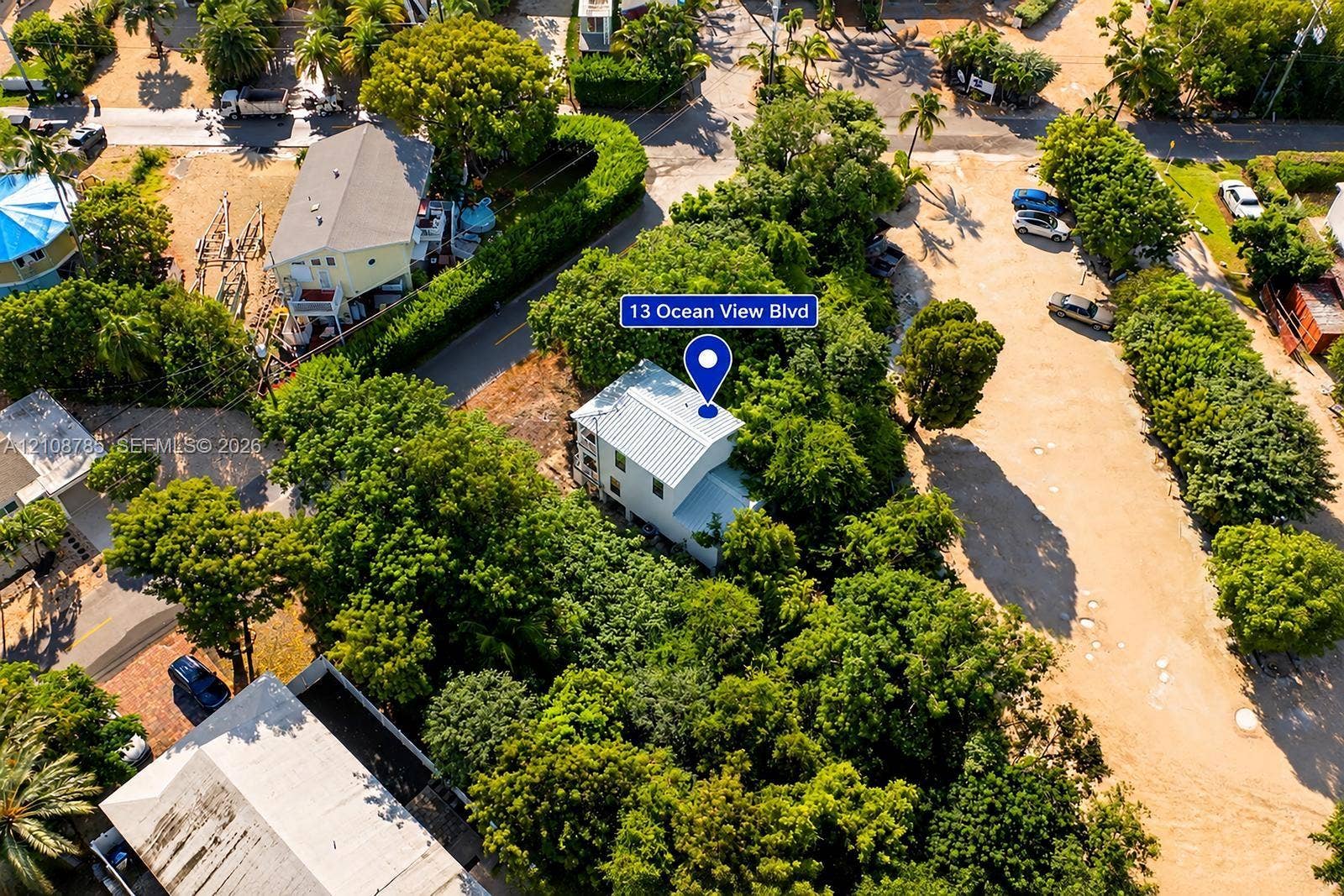 Aerial perspective of a multi-story residence featuring a metal roof, nestled within a lot characterized by mature tree canopy and established vegetation