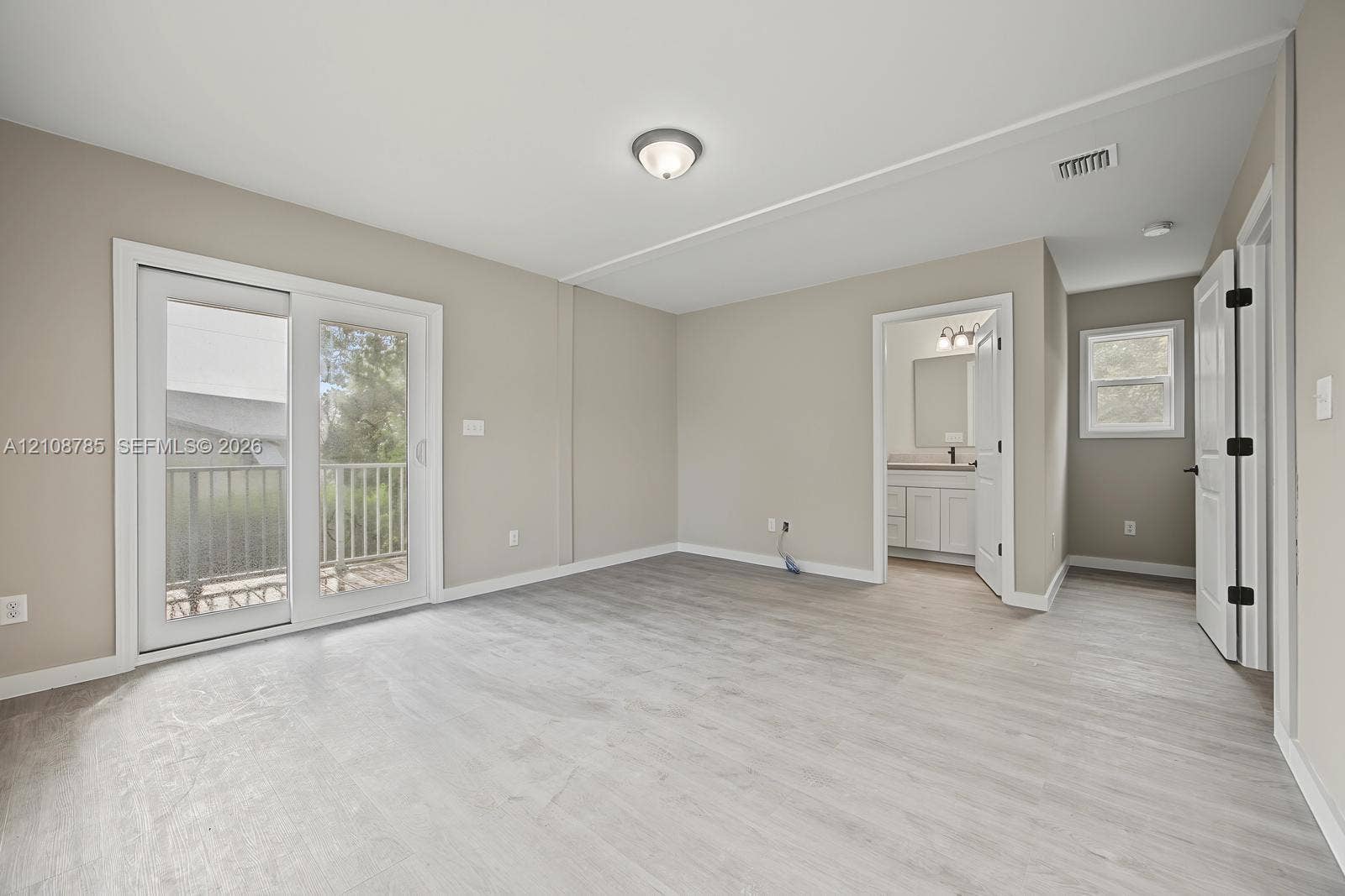 Neutral wall-toned room featuring wood-finish flooring, white sliding glass door, flush-mount ceiling lighting, and crisp white trim