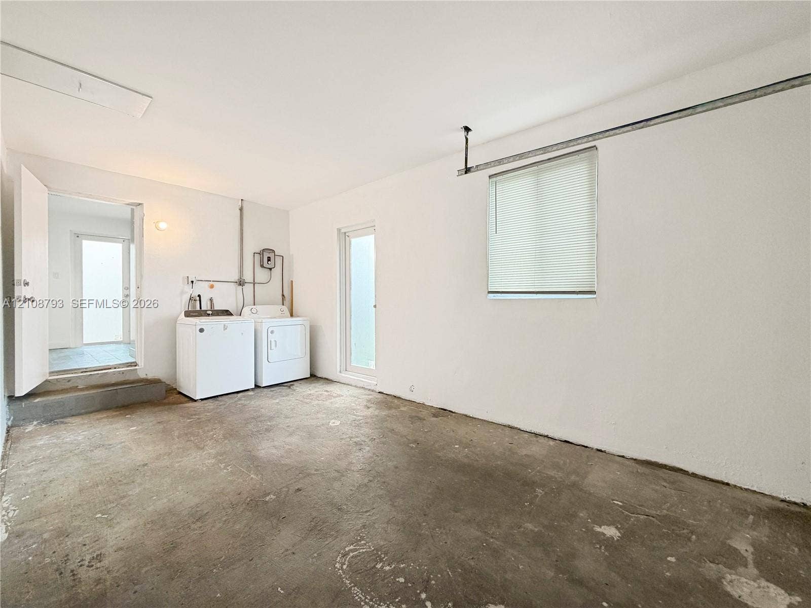 Utility area featuring concrete flooring, white walls, and a window with integrated blinds