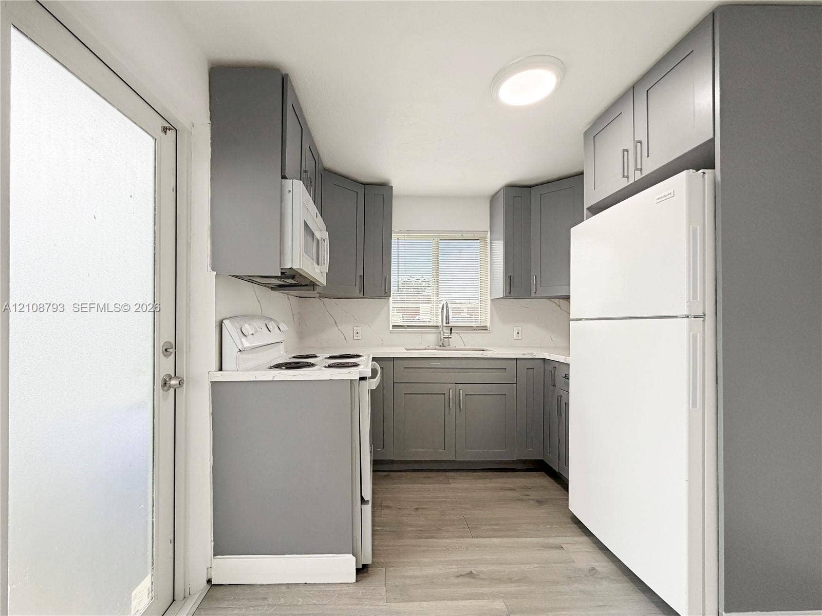 Kitchen featuring grey shaker-style cabinetry, solid-surface countertops with backsplash, wood-finish flooring, and white appliances