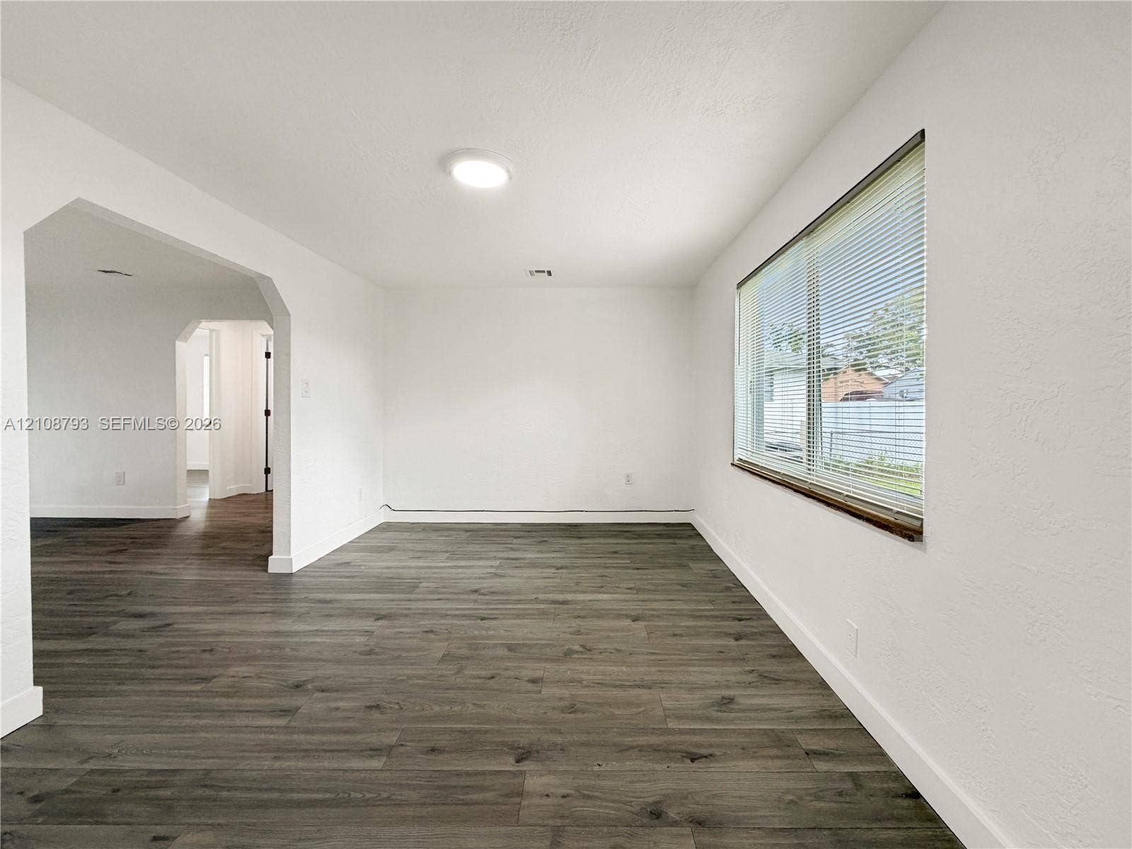 Interior space featuring wood-finish flooring, a large window with horizontal blinds, and a wide arched opening