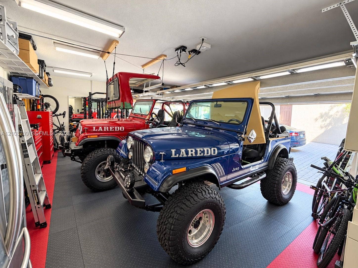 Garage interior featuring modular interlocking flooring, overhead fluorescent lighting, and extensive wall-mounted storage shelving