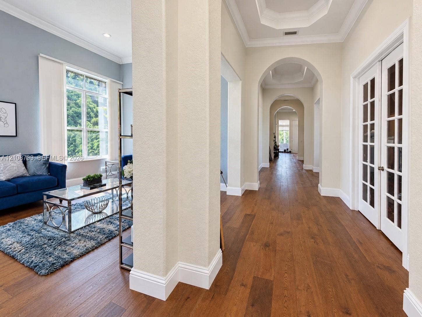 Foyer featuring wood-finish flooring, recessed tray ceilings, arched entryways, and white-trimmed glass-paneled French doors