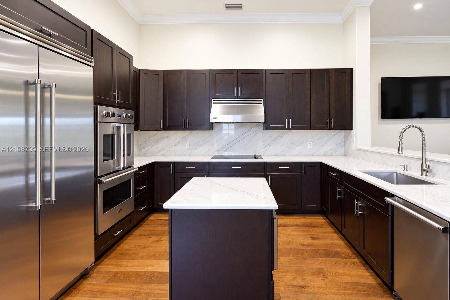 Kitchen featuring dark wood cabinetry, a central island with a stone countertop, stone slab backsplash, stainless steel appliances, and wood-finish flooring