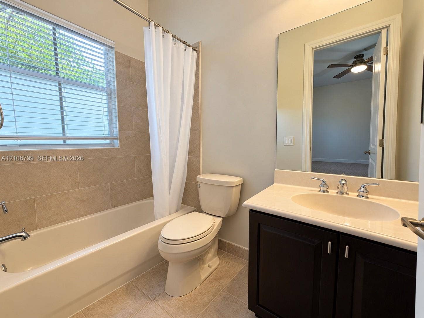 Full bathroom featuring a dark wood-finish vanity with a light-toned countertop, an integrated oval sink, a large wall-mounted mirror, and a tub-shower combination with light-toned horizontal wall tile