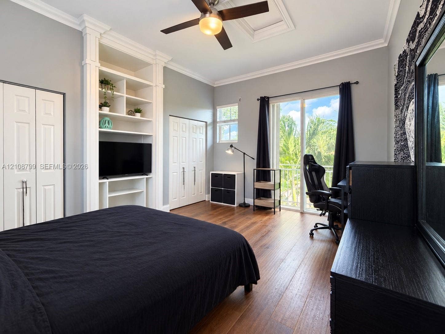 Bedroom featuring wood-finish flooring, custom built-in shelving, double-door closet storage, crown molding, and glass sliding doors