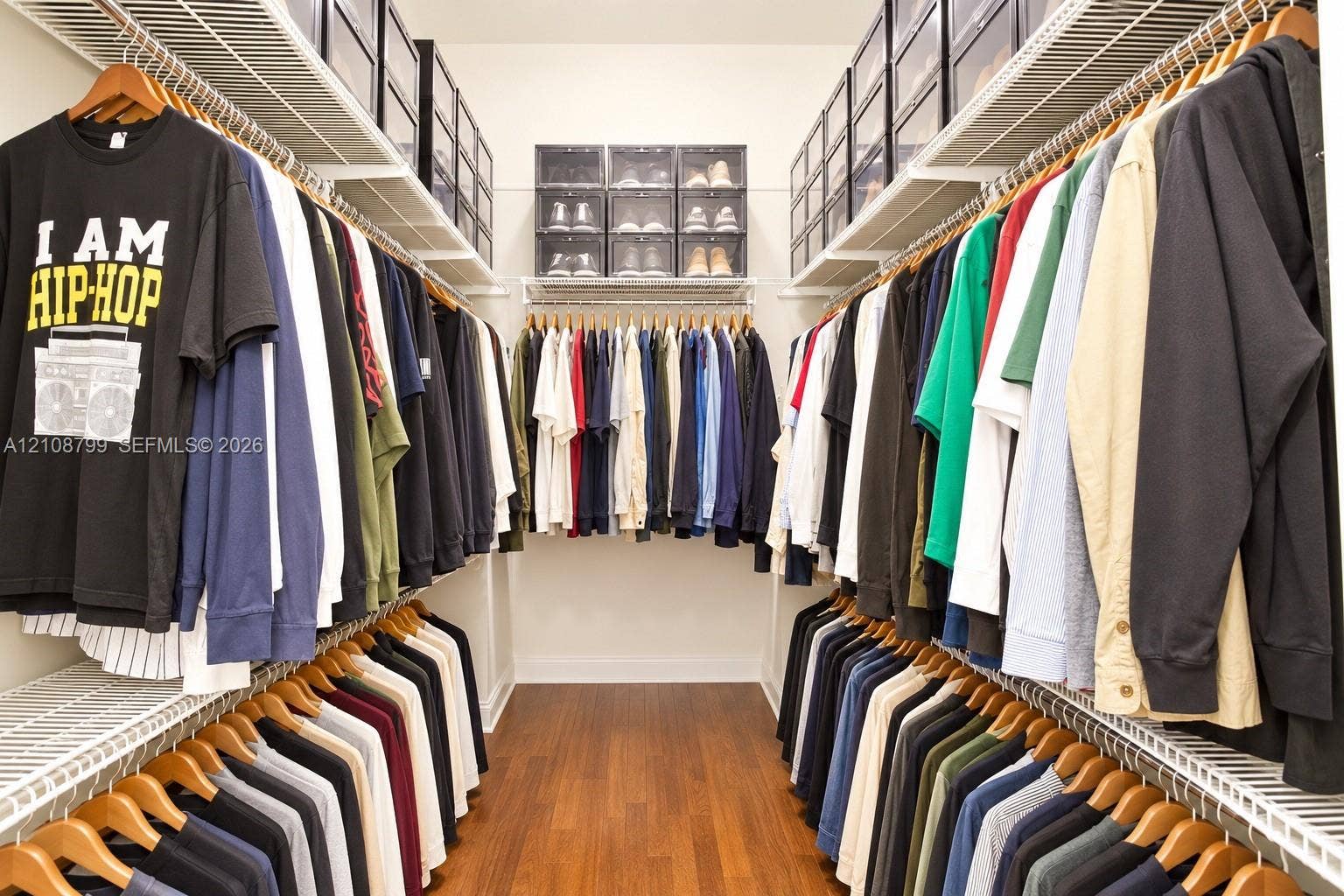 Walk-in closet featuring tiered wire shelving, custom overhead storage compartments, and wood-finish flooring