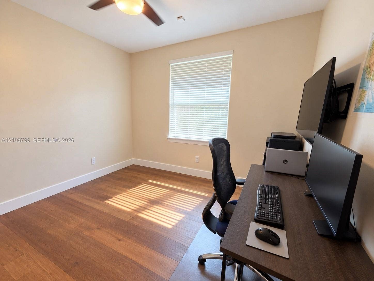 Wood-finish flooring, neutral wall tones, window with horizontal blinds, and a ceiling fan with integrated lighting