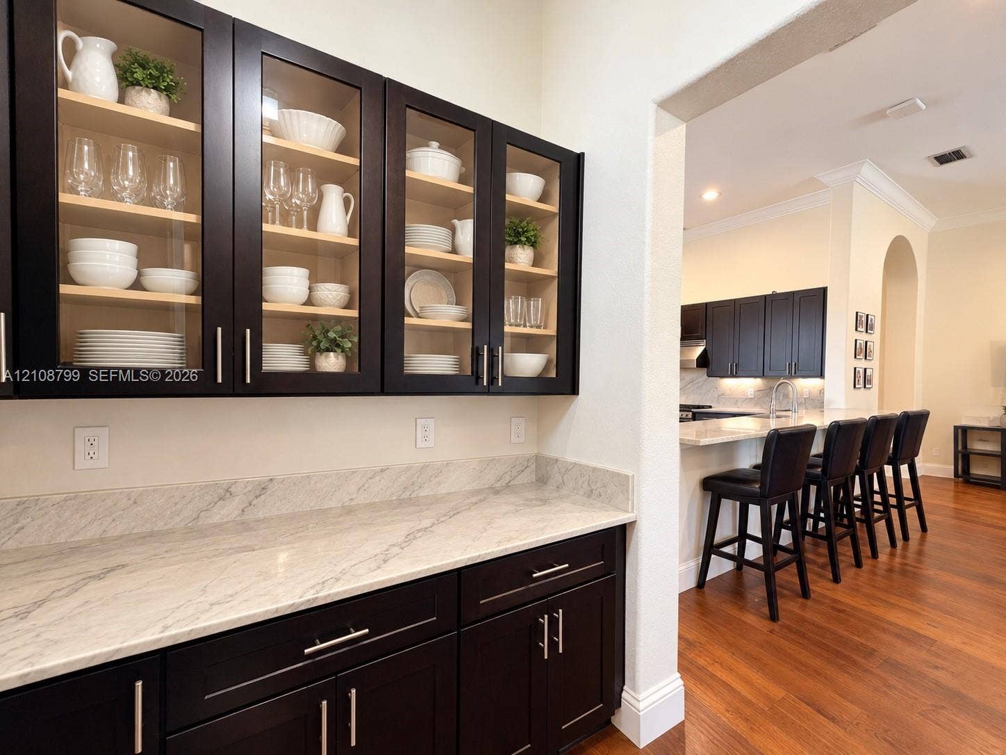 Custom built-in cabinetry featuring glass-front display doors and stone countertops, complemented by dark wood-finish flooring and crown molding