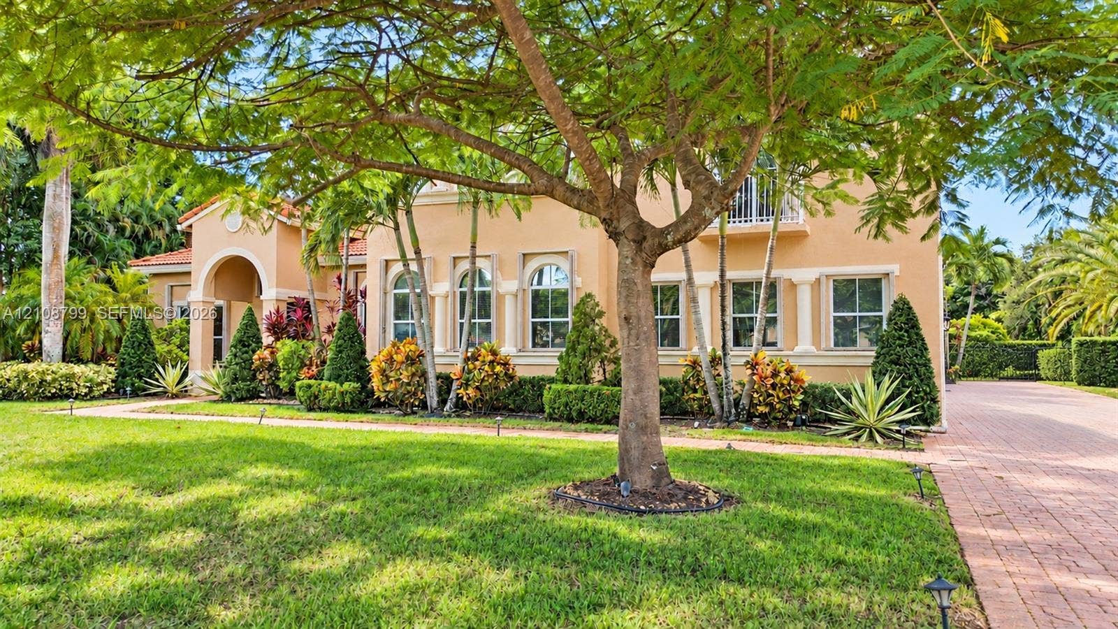 Stucco exterior featuring arched windows, decorative columns, a covered entryway, and a paved driveway