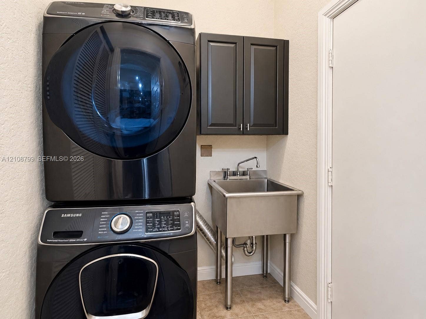 Stacked laundry unit, dark-finish cabinetry, and stainless steel utility sink with gooseneck faucet