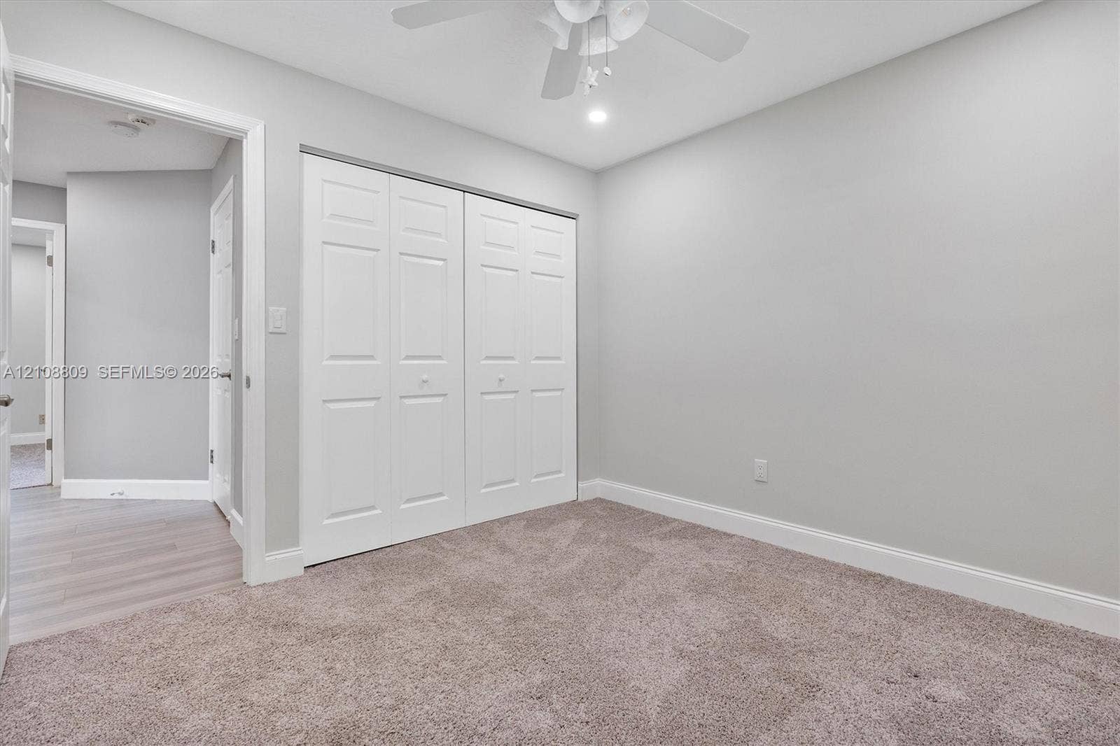 Neutral-toned wall paint, plush carpeting, ceiling fan with integrated lighting, and double-panel closet doors