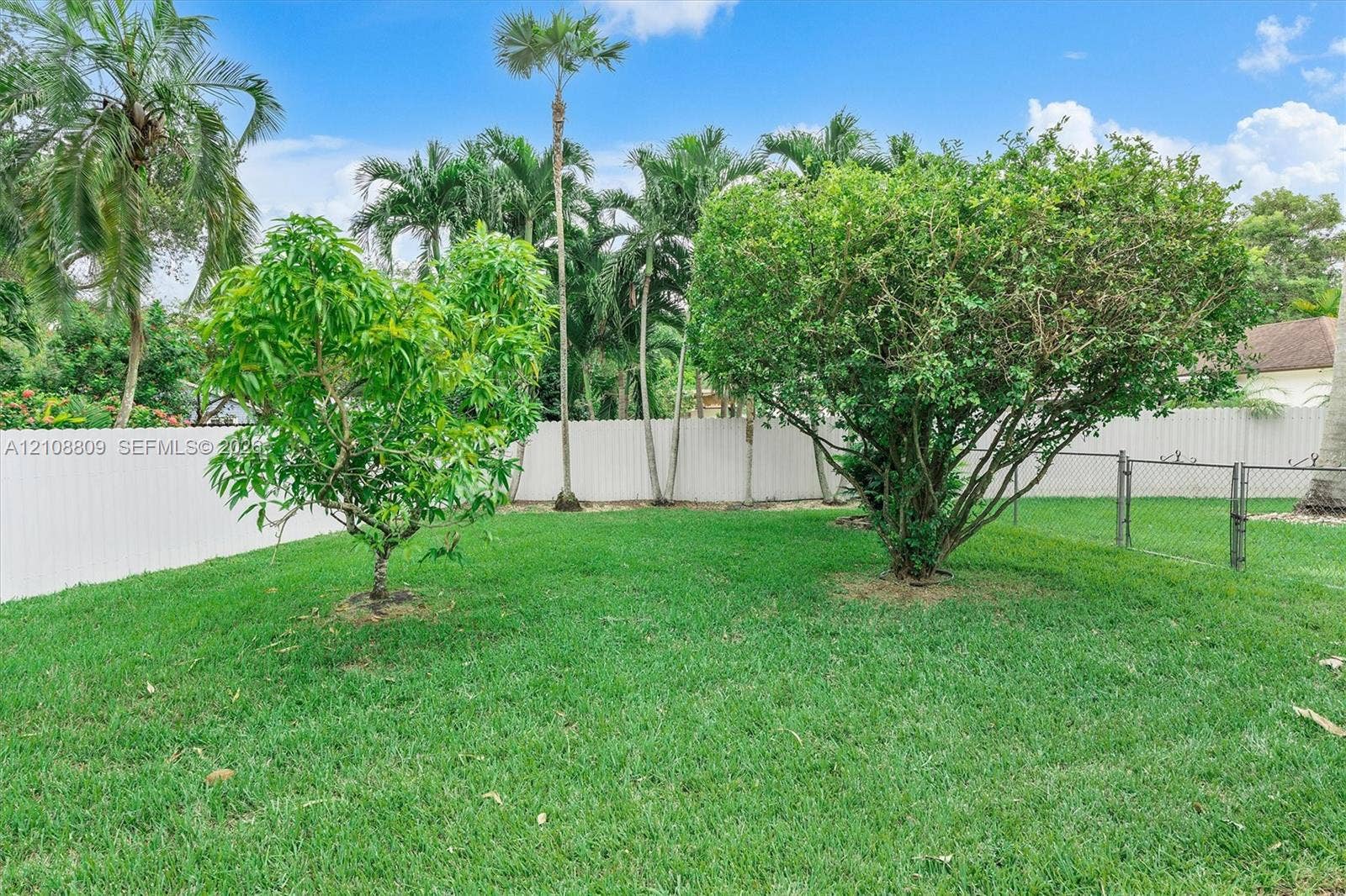 Backyard featuring a grass lawn, mature trees, and white vinyl privacy fencing