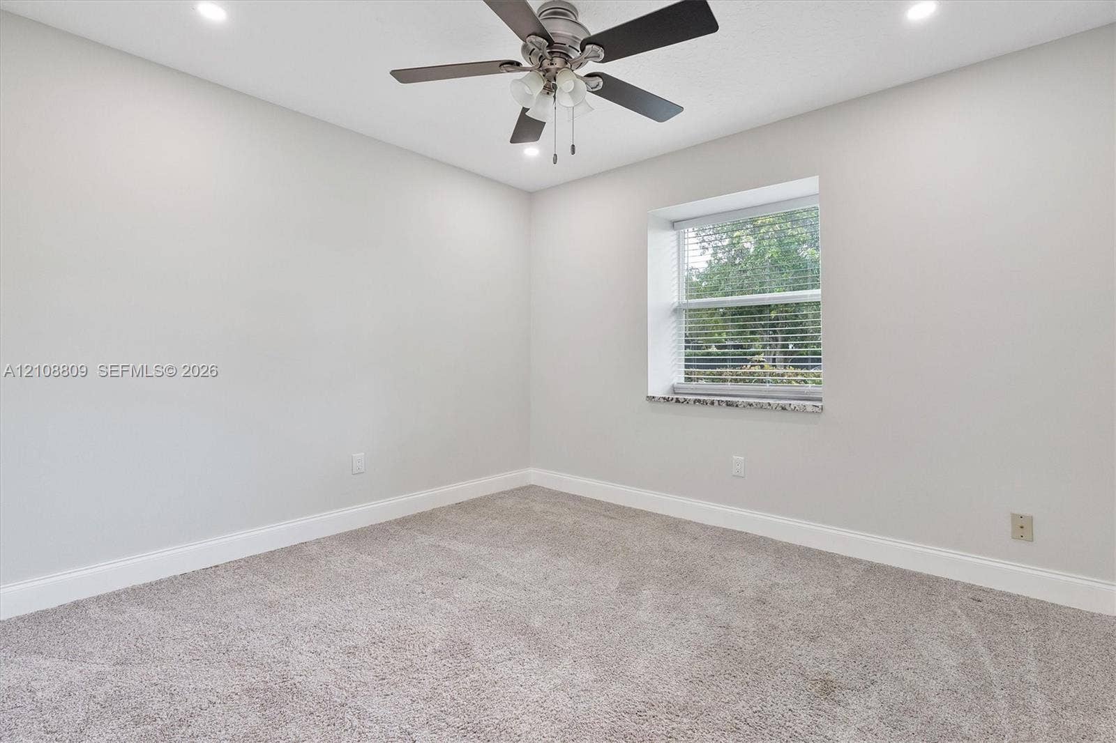 Neutral interior room featuring recessed lighting, a multi-blade ceiling fan with integrated light fixture, neutral carpeting, and a window sill finished in polished stone