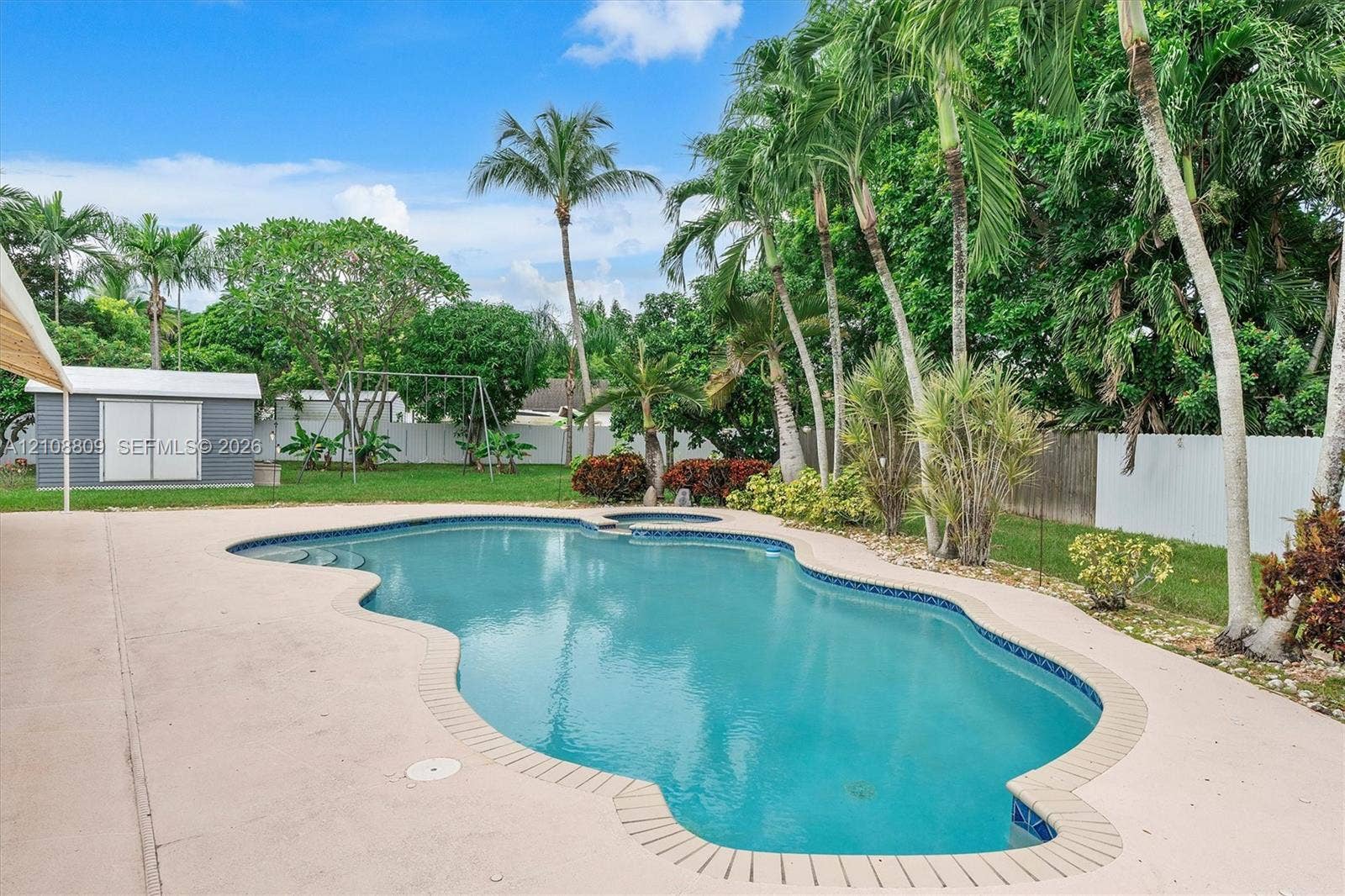Backyard featuring a freeform in-ground swimming pool, integrated spa, concrete deck, and detached storage shed