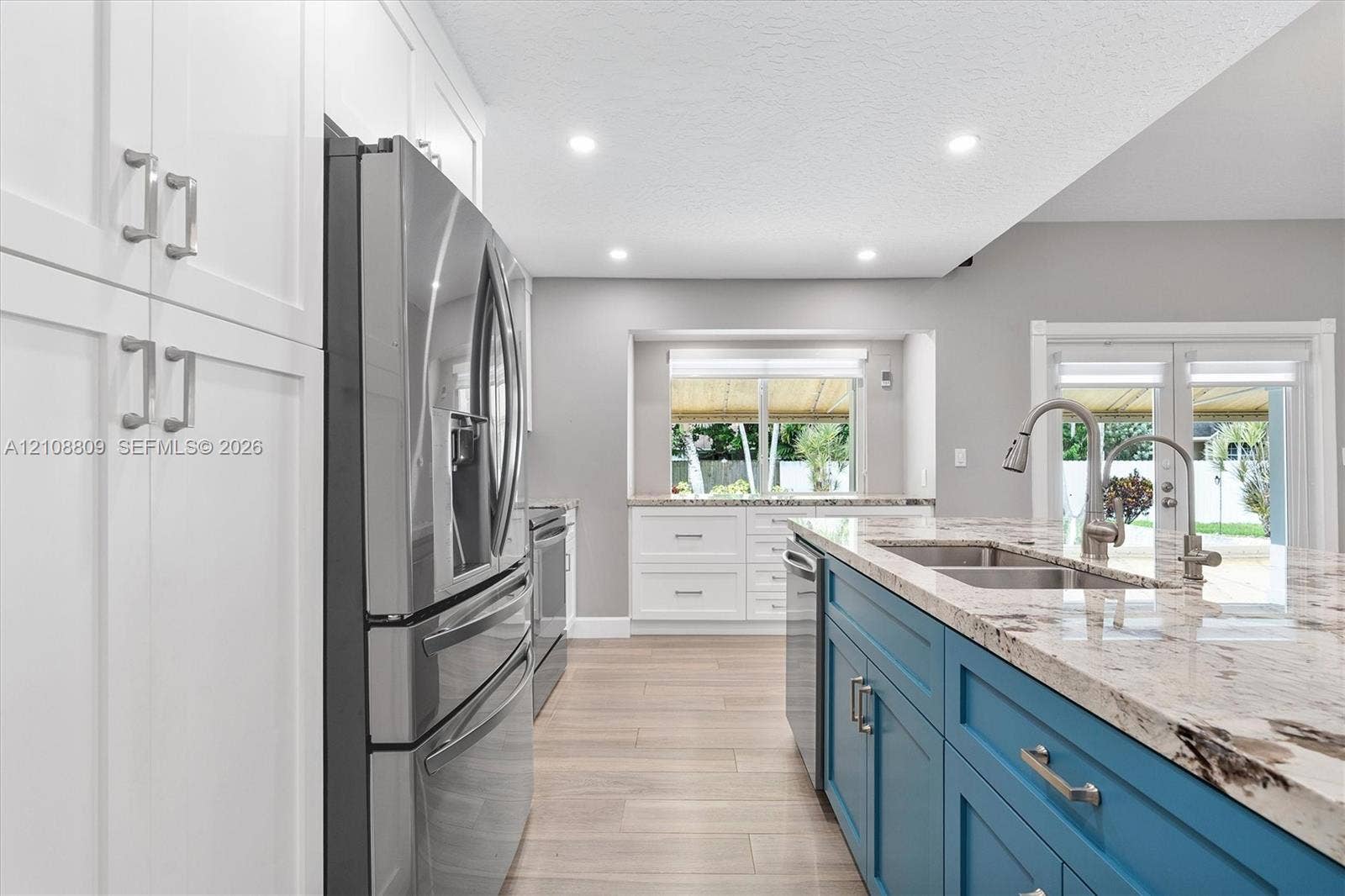 Kitchen featuring white shaker-style cabinetry, blue center island with stone countertop, stainless steel appliances, recessed ceiling lighting, and wood-finish flooring